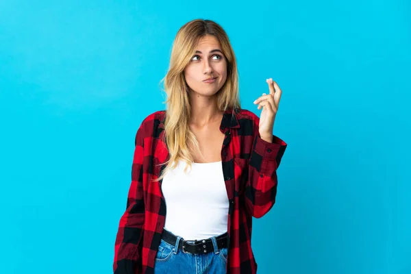 Young blonde Uruguayan woman over isolated background with fingers crossing and wishing the best