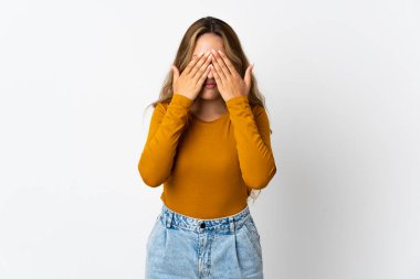 Mavi arka planda izole edilmiş genç sarışın kadın gözlerini elleriyle kapatıyor.
