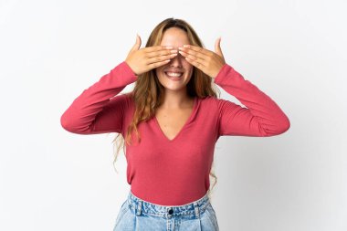 Mavi arka planda izole edilmiş genç sarışın kadın gözleri elleriyle kaplıyor ve gülümsüyor.