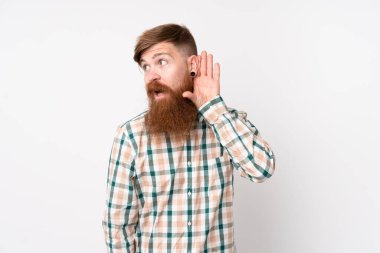 Uzun sakallı, soyutlanmış beyaz arka planda kızıl saçlı bir adam. Kulağına elini sürerek bir şeyler dinliyor.