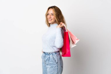Beyaz arka planda izole edilmiş genç sarışın kadın alışveriş torbaları tutuyor ve gülümsüyor.