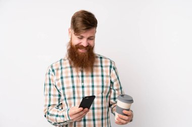 Kızıl saçlı, uzun sakallı, izole edilmiş beyaz arka planı olan, elinde kahve ve cep telefonu olan bir adam.