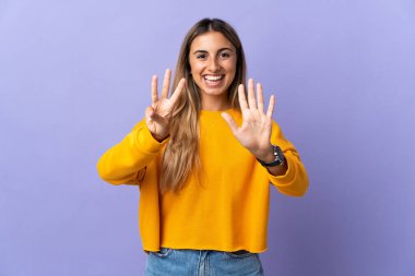 İzole edilmiş mor arka planda genç İspanyol kadın parmaklarıyla sekiz sayıyor.