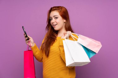 Mor arka planda kalan kızıl saçlı genç kız elinde alışveriş torbalarıyla bir arkadaşına cep telefonuyla bir mesaj yazıyor.