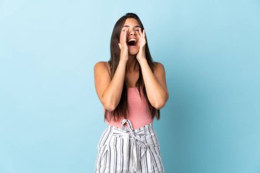 Genç Brezilyalı bir kadın mavi arka planda izole edilmiş bağırıyor ve bir şeyler söylüyor.