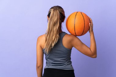 İzole edilmiş mor arka planda basketbol oynayan genç İspanyol kadın.
