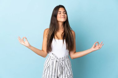 Genç Brezilyalı kadın Zen pozunda mavi arka planda izole edilmiş.