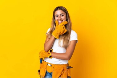 Genç İspanyol elektrikçi kadın izole edilmiş sarı duvarın üzerinden yan tarafa bakıyor ve gülümsüyor.
