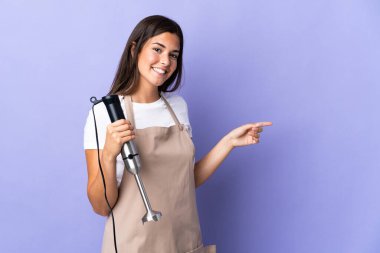 Mor arka planda izole edilmiş el blenderi kullanan Brezilyalı bir kadın.