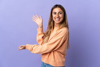 İzole edilmiş mor arka planda genç bir İspanyol kadın davet etmek için ellerini yana uzatıyor.
