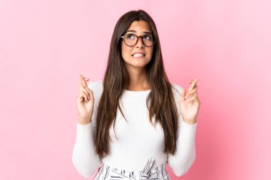 Pembe arka planda izole edilmiş genç Brezilyalı kadın parmaklarını çapraz yapıp en iyisini diliyor.