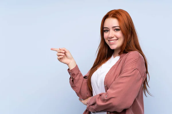 Pelirroja Adolescente Chica Sobre Aislado Azul Fondo Apuntando Dedo Lado —  Fotos de Stock