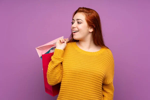 赤毛ティーン女の子上の隔離された紫色の背景を保持ショッピングバッグと振り返って — ストック写真