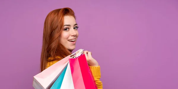 赤毛ティーン女の子上の隔離された紫背景を保持ショッピングバッグと笑顔 — ストック写真