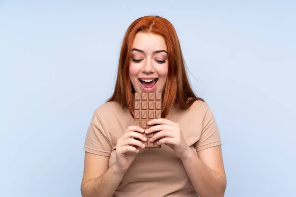 Redhead Teenager Girl Isolated Blue Background Eating Chocolate Tablet — Stock Photo, Image