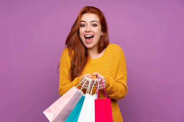 赤毛ティーン女の子上の隔離された紫背景保持ショッピングバッグと驚き — ストック写真