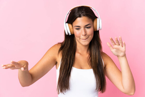 Young brazilian girl isolated on pink background listening music and dancing