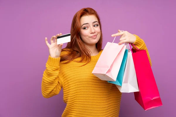 Redheadティーン女の子上の隔離された紫背景保持ショッピングバッグとクレジットカード — ストック写真