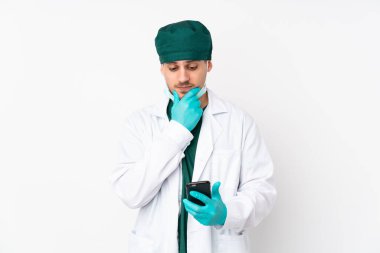 Yeşil üniformalı cerrah, izole edilmiş beyaz arka planda düşünüp bir mesaj gönderiyor.