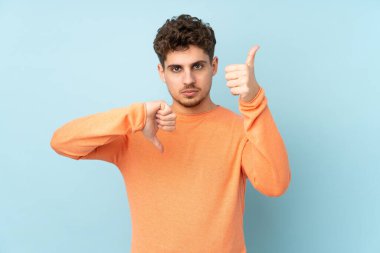 Beyaz adam mavi arka planda izole edilmiş, iyiye kötüye işaret yapıyor. Evet ya da hayır arasında kararsız