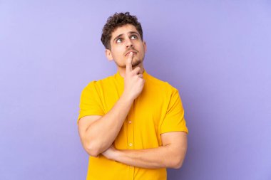 Kafkasyalı adam mor arka planda izole edilmiş, yukarı bakarken şüpheleri var.