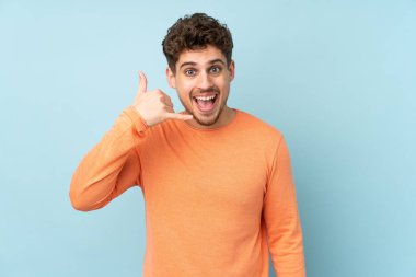 Beyaz adam mavi arka planda izole edilmiş bir şekilde telefon jesti yapıyor. Bana geri dönüş işareti ver.