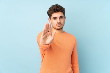 Beyaz adam mavi arka planda izole edilmiş. Durma hareketi yapıyor.