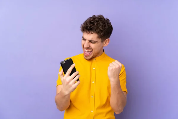 Hombre Caucásico Aislado Sobre Fondo Púrpura Con Teléfono Posición Victoria —  Fotos de Stock