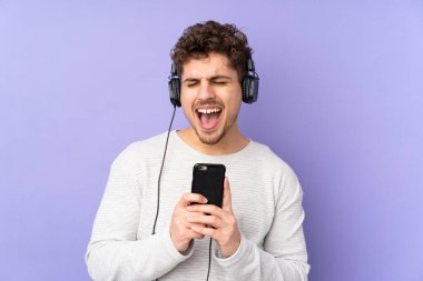 Mor arka planda izole edilmiş beyaz bir adam cep telefonuyla müzik dinliyor ve şarkı söylüyor.