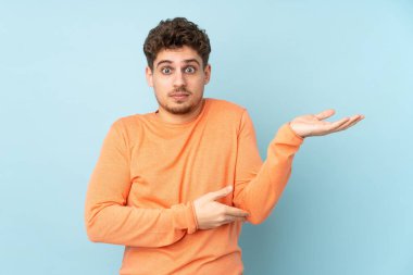 Kafkasyalı adam mavi arka planda izole edilmiş. Bir şeyi anlamadığı için mutsuz.