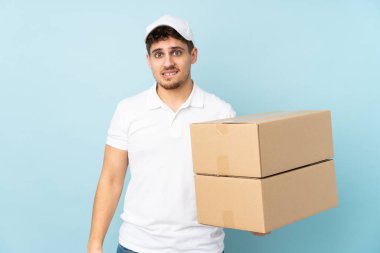 Teslimatçı beyaz adam mavi arka planda izole edilmiş. Şüpheleri var ve kafası karışmış bir yüz ifadesi var.