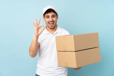 Teslimatçı beyaz adam mavi arka planda izole edilmiş. Parmaklarıyla 