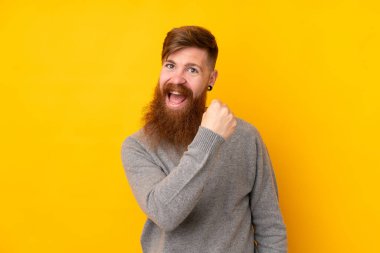 Kızıl saçlı, uzun sakallı, izole edilmiş sarı arka planlı bir adam zaferi kutluyor.