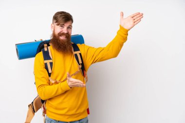 İzole edilmiş beyaz arka plan üzerinde büyük bir sırt çantası olan genç dağcı, davet edilmek için ellerini yana uzatıyor.