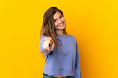 Sarı arka planda izole edilmiş genç Slovak kadın mutlu bir ifadeyle ön tarafı işaret ediyor