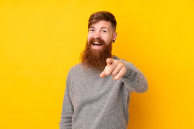 Kızıl saçlı, uzun sakallı, izole edilmiş sarı arka planı olan, şaşırmış ve ön tarafı işaret eden bir adam.