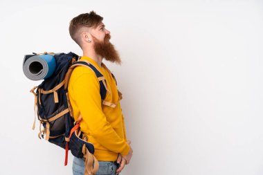 İzole edilmiş beyaz arka plan üzerinde büyük bir sırt çantası olan genç dağcı yan tarafa bakıyor.