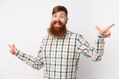 Uzun sakallı, soyutlanmış beyaz arka planı olan kızıl saçlı adam parmak uçlarını işaret ediyor ve mutlu.