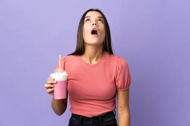 Genç kız elinde çilekli milkshake ile yukarı bakıyor ve şaşırmış bir ifadeyle