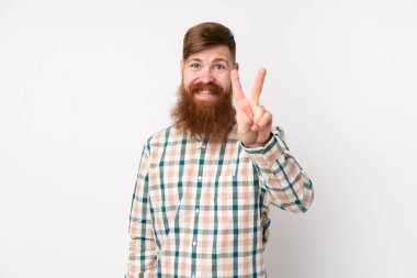 Uzun sakallı kızıl saçlı adam izole edilmiş beyaz arka planda gülümsüyor ve zafer işareti gösteriyor.