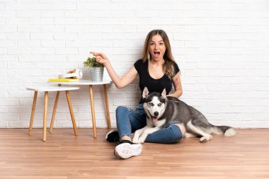 Genç ve güzel bir kadın, köpeğiyle yerde oturuyor. Kapalı alanda şaşkın şaşkın oturuyor.