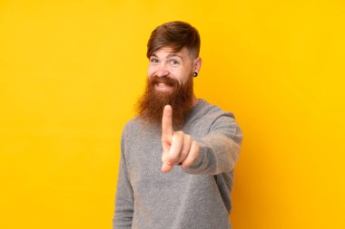 Sarı arka planda uzun sakallı kızıl saçlı adam parmağını kaldırıyor ve gösteriyor.