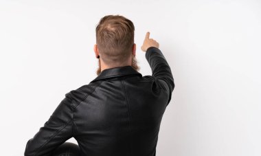 Uzun sakallı, motosikletli bir kaskla izole edilmiş beyaz arka planı olan kızıl saçlı adam işaret parmağıyla işaret ediyor.