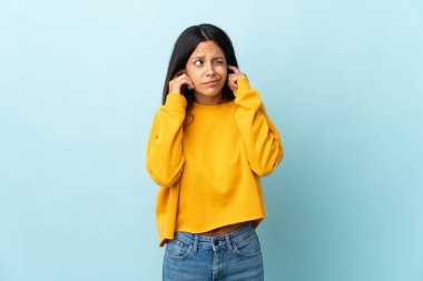 Mavi arka planda izole edilmiş beyaz kız hayal kırıklığına uğramış ve kulaklarını kapatmış.