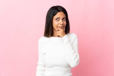 Pembe arka planda izole edilmiş beyaz bir kız. Şüpheleri var ve kafası karışmış bir yüz ifadesi var.