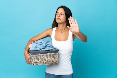 Arka planda bir çamaşır sepetini tutan genç bir kadın dur hareketi yapıyor ve hayal kırıklığına uğruyor.