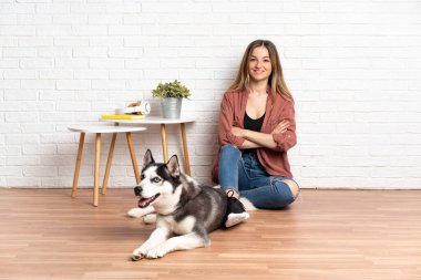 Köpeğiyle birlikte evde oturmuş gülümseyen genç bir kız.