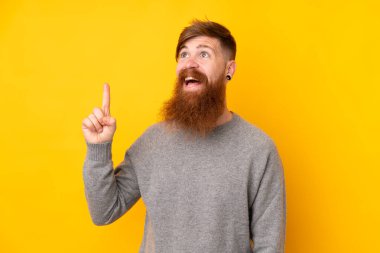 Kızıl saçlı, uzun sakallı, izole edilmiş sarı arka planlı adam yukarı bakıyor ve şaşırıyor.