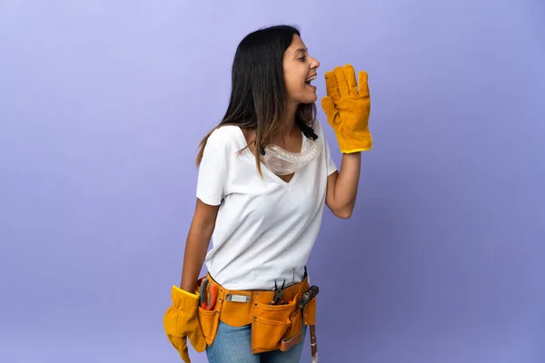 Young electrician woman isolated on purple background shouting with mouth wide open to the side