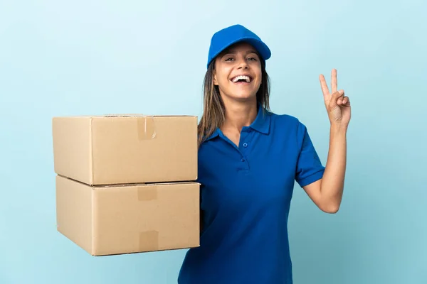 Young delivery woman isolated on blue background smiling and showing victory sign